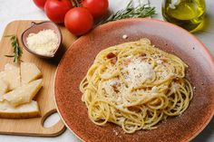 a plate of spaghetti with cheese, bread and tomatoes on a table next to olives