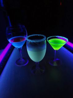 three different colored drinks sitting next to each other in front of a neon light background