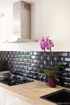 a kitchen with a stove top oven next to a vase filled with purple orchids