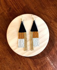 two tone tasseled earrings with gold and black beads on a white marble plate