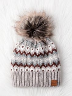 a knitted hat with a pom - pom on top sitting on white fur