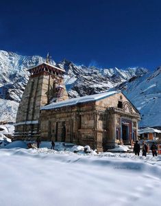 an old building with snow on the ground and mountains in the background