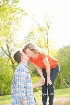 a couple kissing in the park during their engagement photo session with trees in the background