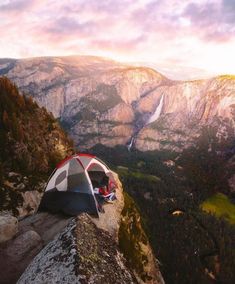 a tent pitched up on the side of a cliff with mountains in the background at sunset