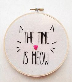 the time is meow embroidered on a white hoop with black lettering and a pink heart