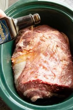 a person is pouring seasoning into a large piece of meat in a green bowl