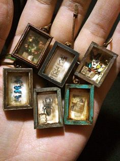 a person's hand holding five miniature frames with pictures in them, all hanging from chains