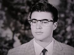 a black and white photo of a young man wearing glasses, a suit and tie