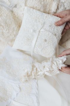 a person is holding a pillow on top of some white lace and satin materials