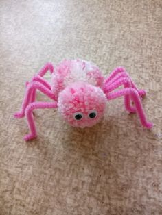 a close up of a pink spider on the ground with eyes and legs made out of pom poms