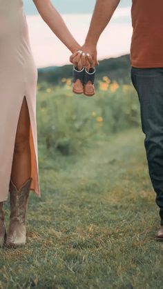 a man and woman holding hands while walking through the grass with boots on their feet