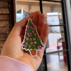 a hand holding a sticker with a christmas tree on it