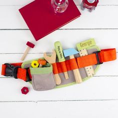 an assortment of wooden toys and tools laid out on a white table next to a red book