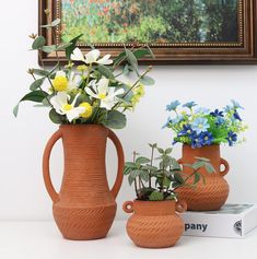 three clay vases with flowers in them sitting on a table next to a book