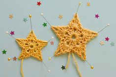 two crocheted stars with pins attached to them on a light blue surface surrounded by small beads