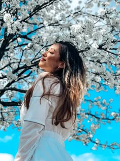 a woman standing in front of a tree with white flowers