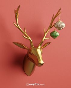 a golden deer head with ornaments hanging from it's antlers on a pink background