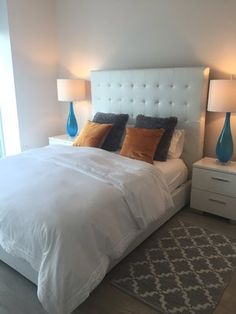 a white bed sitting next to two lamps on either side of a window in a bedroom