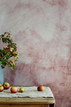 a vase filled with apples sitting on top of a wooden table next to a wall