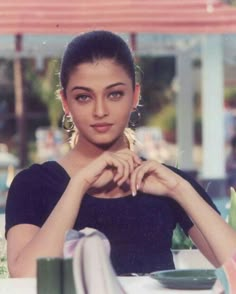 a young woman sitting at a table with her hands on her heart shaped fingernail