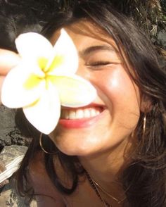 a woman holding a flower in front of her face while she smiles at the camera