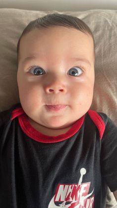 a baby with big blue eyes laying on top of a bed looking at the camera