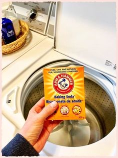 a person holding a box of baking soda in front of a washing machine