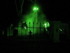 a green light shines in the dark over a cemetery at night with an iron fence