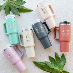 six travel mugs sitting next to each other on a white towel with green leaves