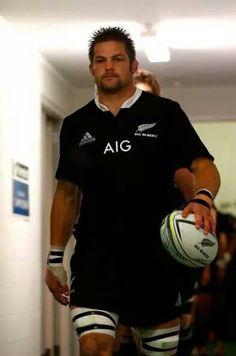 a man holding a rugby ball in his right hand while walking down a hallway with other people