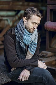 a man sitting on the ground wearing a blue and grey scarf with his hands in his pockets