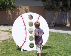 a young boy standing in front of a giant baseball shaped paper plate on the grass