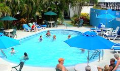 an outdoor swimming pool with people sitting around it and umbrellas over the poolside