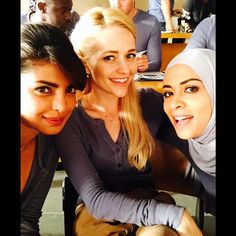 three beautiful young women posing for a photo in front of a group of other people