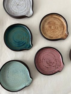 six different colored dishes sitting on top of a white cloth covered tablecloth, with one empty bowl in the middle