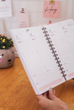 a person holding a planner in their hand on top of a wooden table next to a potted plant