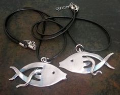 two silver fish pendants sitting on top of a black leather cord next to each other