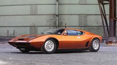 an orange sports car is parked in front of a large industrial building with steel grates on the walls