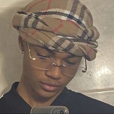 a young man wearing glasses and a burluck hat looking at his cell phone