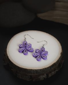 two purple flowers are sitting on top of a piece of wood, next to a pair of earrings