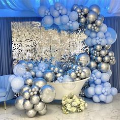 a bathtub filled with lots of silver balloons and flowers on top of a marble floor