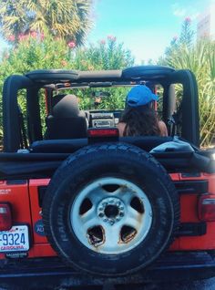 a woman is sitting in the back of a red jeep with her hat on and looking at palm trees