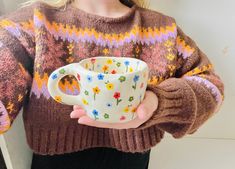 a woman is holding a coffee cup in her right hand and wearing a sweater with flowers on it