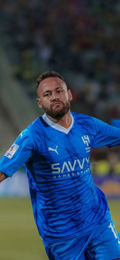 the soccer player is wearing blue and has his arm out in front of him as he prepares to kick the ball