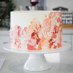 a white cake with pink and orange flowers on it sitting on a plate in the kitchen