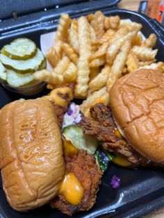 a sandwich and fries are on a black plastic tray, with pickles in the background