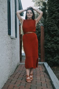 a woman in a red dress is standing on a brick walkway with her hands behind her head