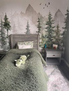 there is a bed with a green comforter on it and trees painted on the wall