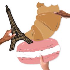 two hands holding up a paper cutout of the eiffel tower and doughnut