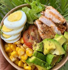 a bowl filled with meat, vegetables and hard boiled eggs on top of corn next to lettuce